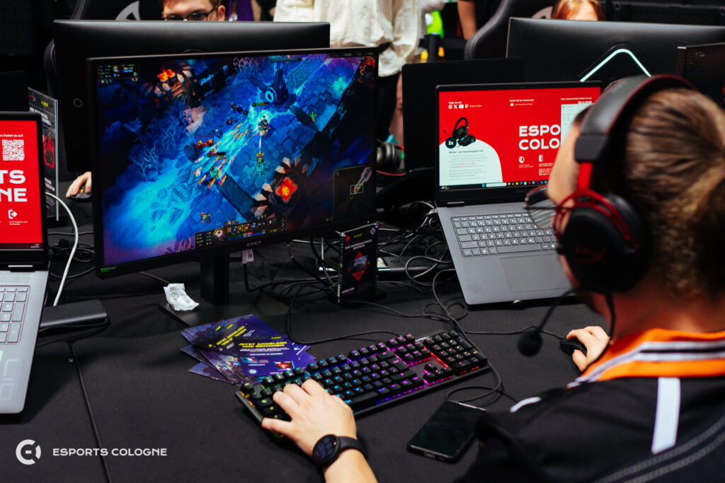 Jemand spielt League of Legends, während auf einem 2. Bildschirm Informationen zu eSports Cologne zu sehen sind