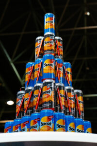 Aus Spezi Original und Spezi Zero Dosen aufgebaute Pyramide mit roten Kugelschreibern auf einer Messefläche. Die Getränkepyramide dient als Blickfang für Besucherinnen und Besucher.